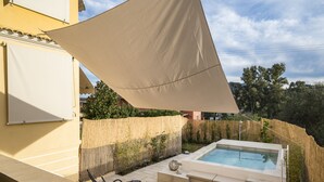 Un espace extérieur privé avec piscine, un jacuzzi, des chaises longues et une grande voile d’ombrage.