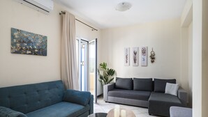 Un salon avec un canapé bleu, un canapé gris et une table basse sur laquelle sont posées des bougies. On y trouve également une plante et des œuvres d’art accrochées aux murs.