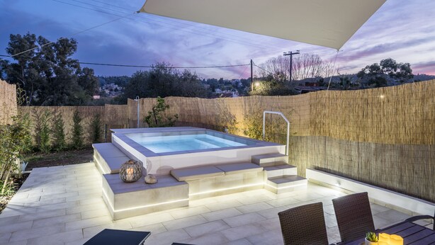 Un espace extérieur aménagé avec un jacuzzi, accessible par des marches, entouré d’une clôture en bois et surmonté d’un grand auvent.