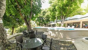 Un área de piscina al aire libre con sillones de descanso y una mesa de comedor rodeada de árboles.