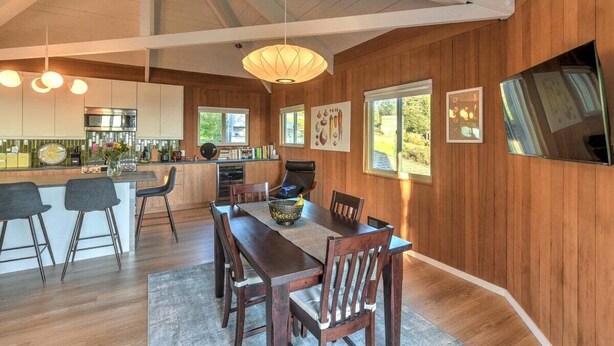A spacious kitchen with modern appliances, a dining area with wooden furniture, and large windows providing natural light.