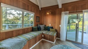 A wooden interior with a bench seating area, large windows, and a sliding glass door.