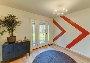 A room with a dark blue cabinet, a potted plant, a geometric-patterned rug, and a wall with a large red chevron design. - Stellar View | Panoramic Ocean Views & Hot Tub (Sea Ranch)