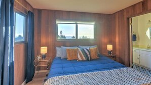 A bedroom with a large bed, two bedside tables, a window with curtains, and a view of the outdoors.