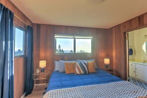 A bedroom with a large bed, two bedside tables, a window with curtains, and a view of the outdoors.
