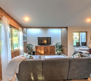 A modern living room with a large sectional sofa, a flat-screen TV, and a desk with a computer. - Stellar View | Panoramic Ocean Views & Hot Tub (Sea Ranch)