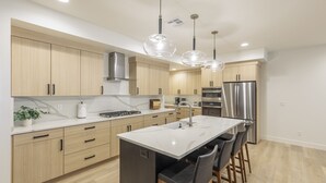 A modern kitchen with wooden cabinets, a central island with bar stools, stainless steel appliances, and pendant lighting. - Modern 3BR, Next to Pool, Hot Tub, Golf Views (St. George)