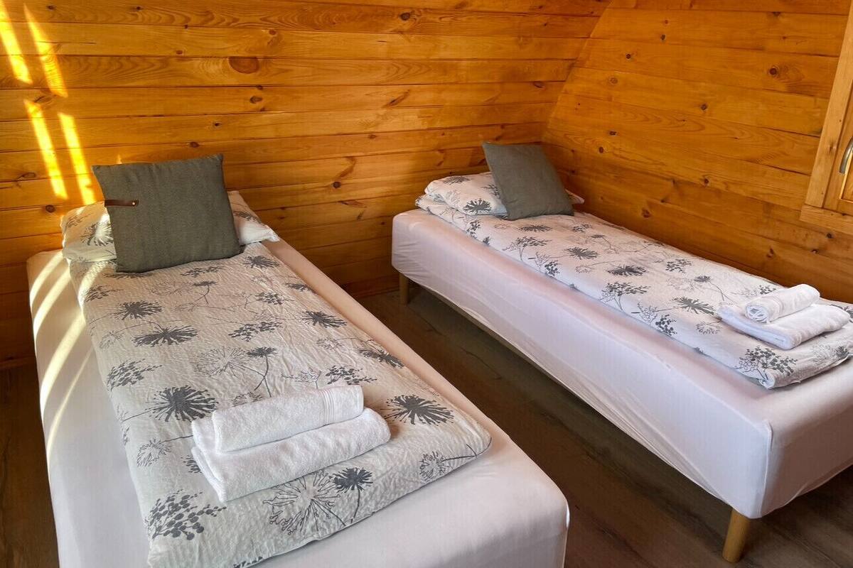 Two single beds with floral bedding and pillows, wooden walls, and a wooden floor.