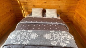 A small, cozy wooden cabin room with a bed, two pillows, and a floral-patterned blanket. - Starlight Camping Pods (Rangárþing eystra)