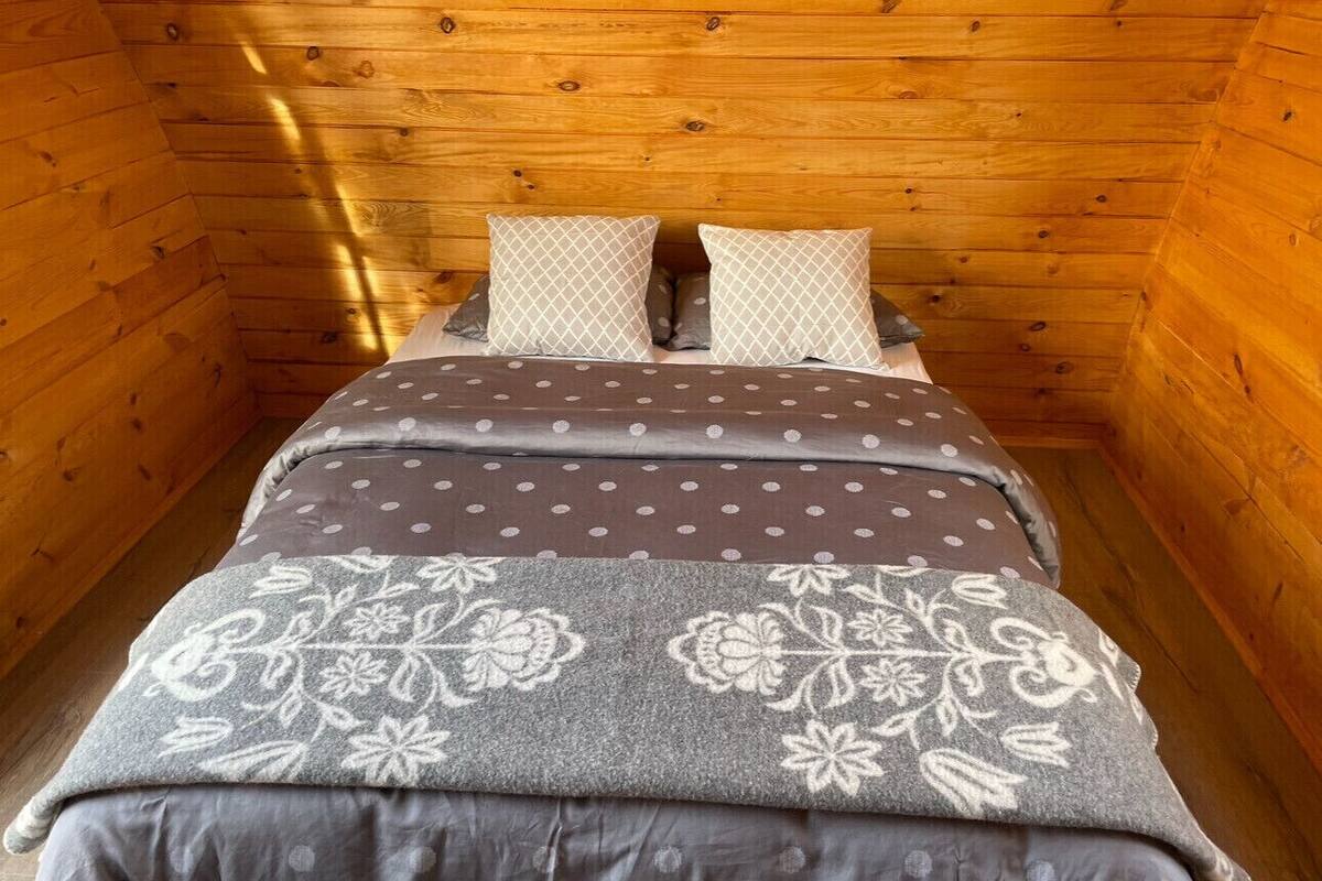A small, cozy wooden cabin room with a bed, two pillows, and a floral-patterned blanket.