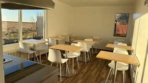 A modern classroom with wooden tables and white chairs, large windows with a view of a field, and a radiator under the windows. - Starlight Camping Pods (Rangárþing eystra)