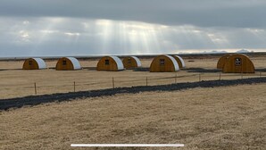 A row of wooden dome-shaped cabins in a dry, open field with a cloudy sky.