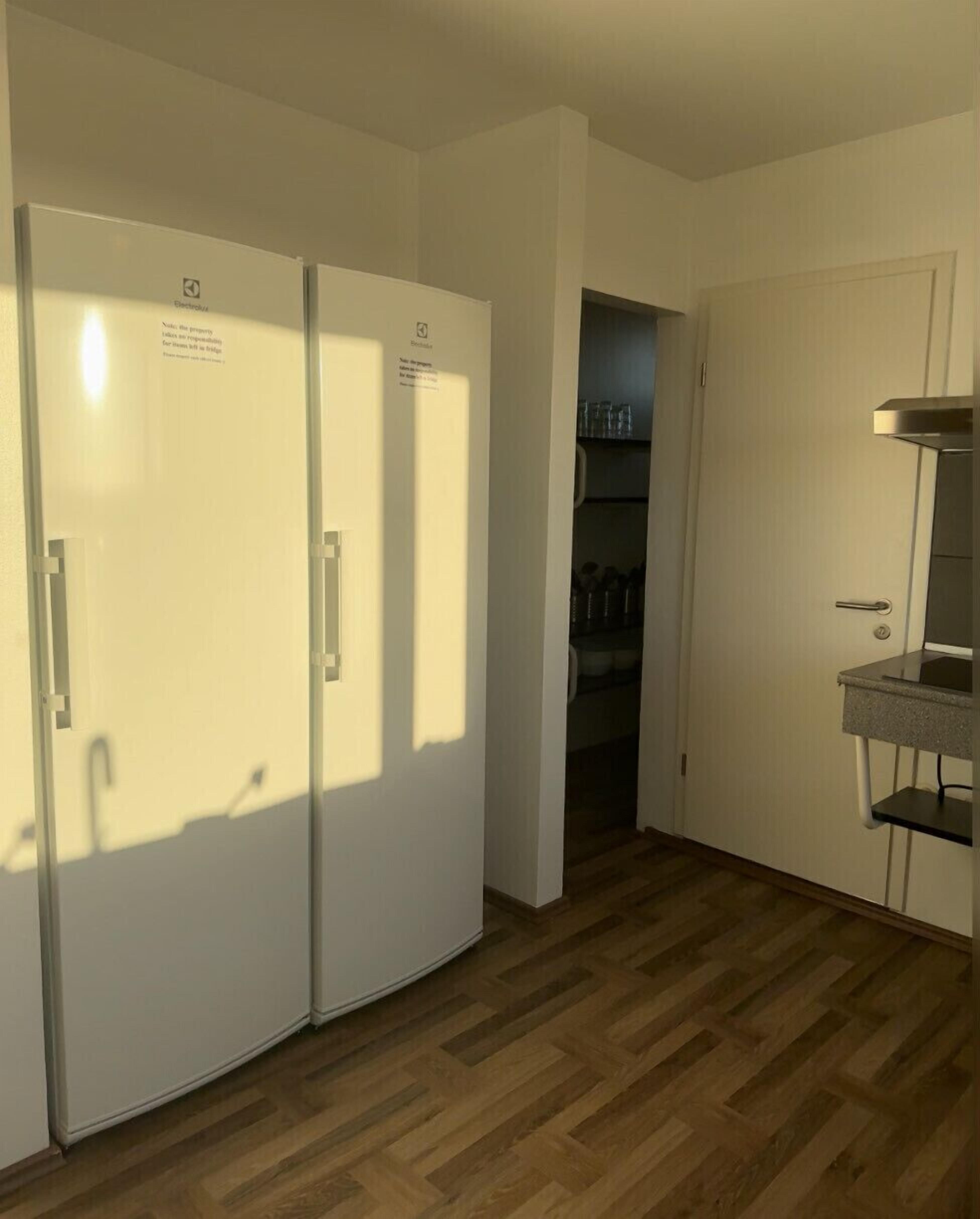 A kitchen with two white refrigerators, a wooden floor, and a small countertop with a sink.