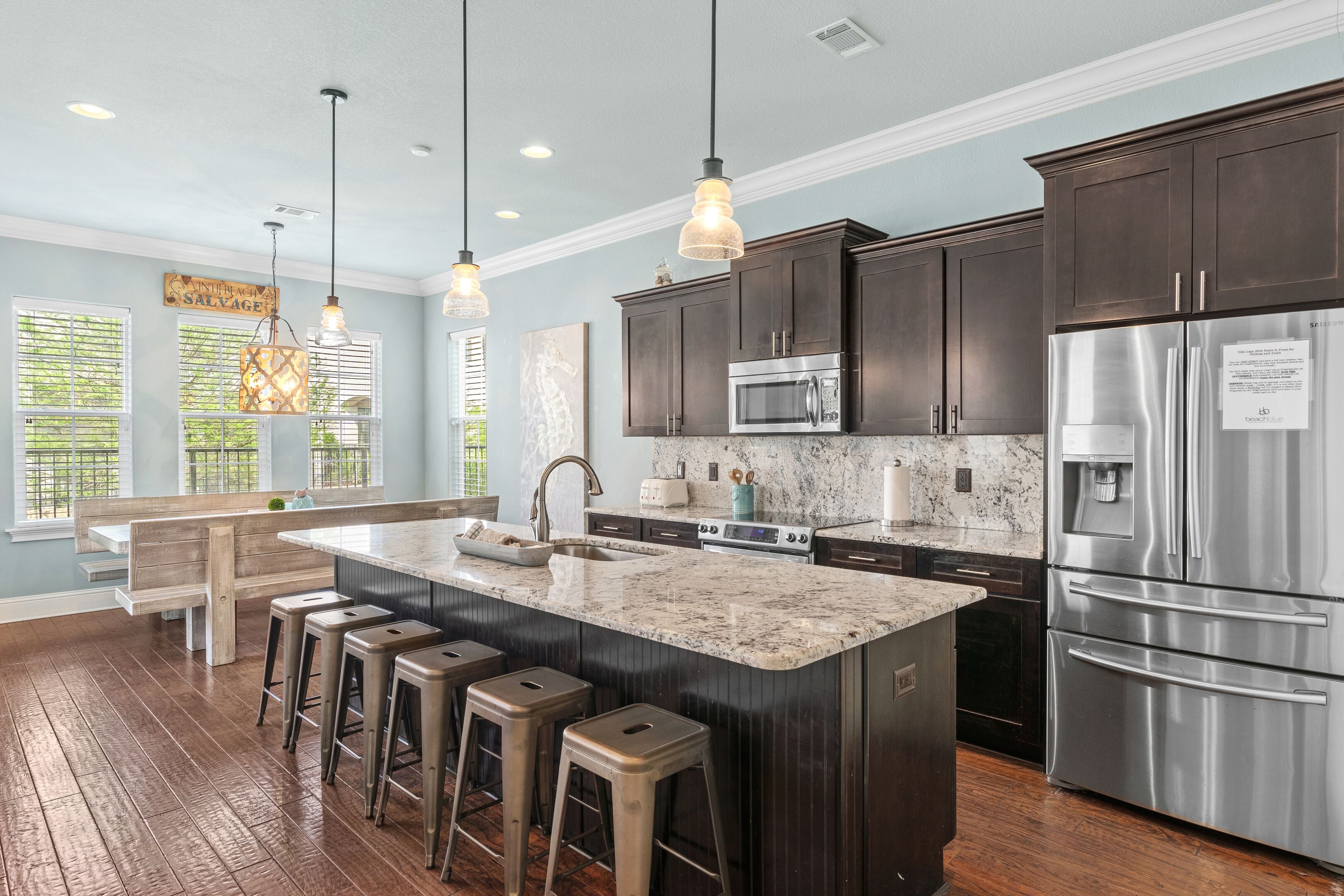 A modern kitchen with dark cabinets, stainless steel appliances, a marble island with bar stools, and pendant lighting.