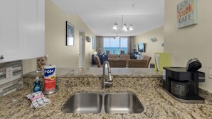 A kitchen with granite countertops, a double sink, and a coffee maker. There is a view of the ocean through large windows. - Stella Marina - Caribbean Resort 502.Bch srvc incl!!! (Navarre)