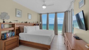 A hotel room with a bed, a desk, a TV, a ceiling fan, and a view of the ocean. - Stella Marina - Caribbean Resort 502.Bch srvc incl!!! (Navarre)
