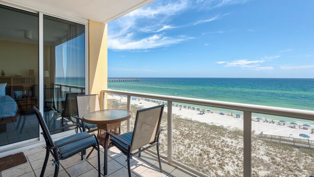 A balcony with a view of the ocean and a pier. There are two chairs and a small table. - Stella Marina - Caribbean Resort 502.Bch srvc incl!!! (Navarre)