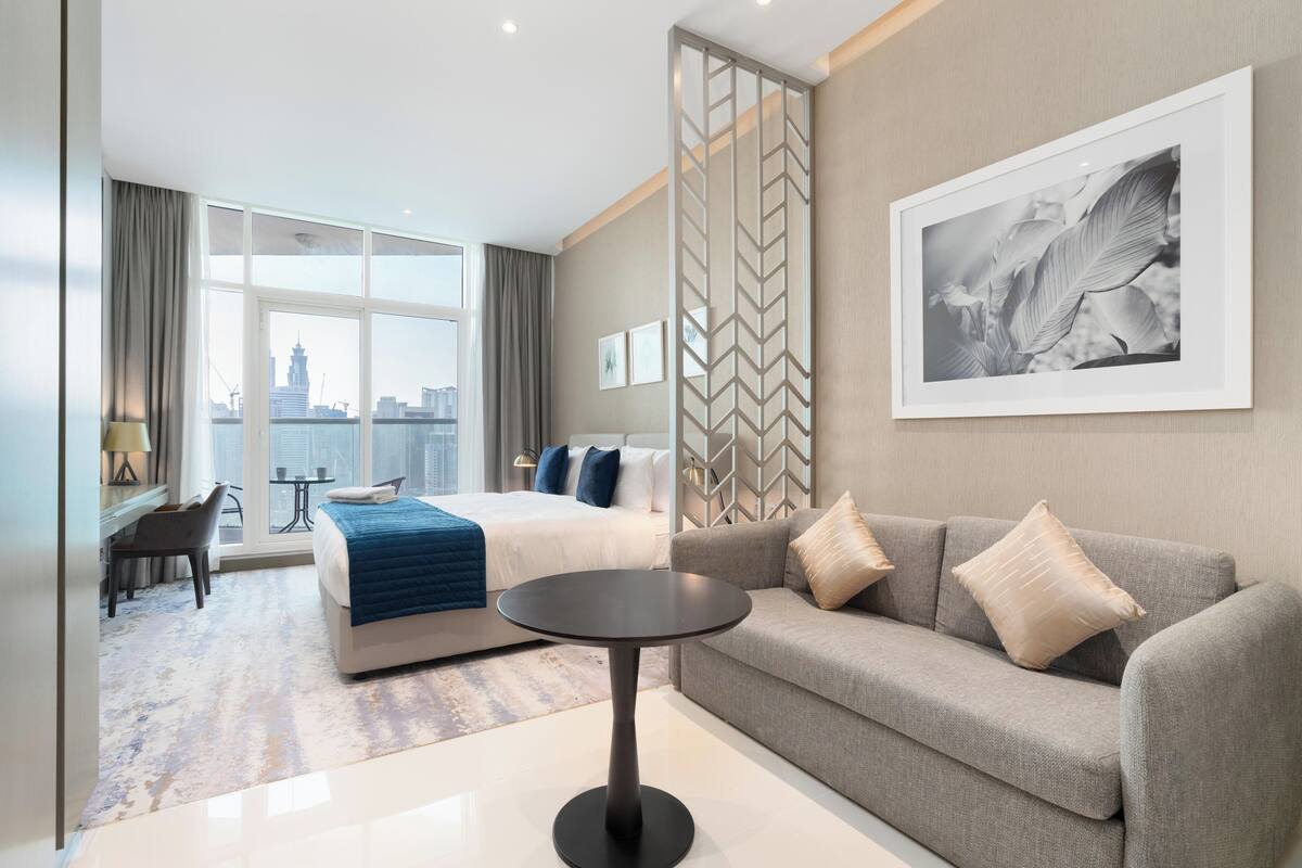 Ein modernes Hotelzimmer mit Bett, Sofa, rundem Tisch und Blick auf die Stadt.