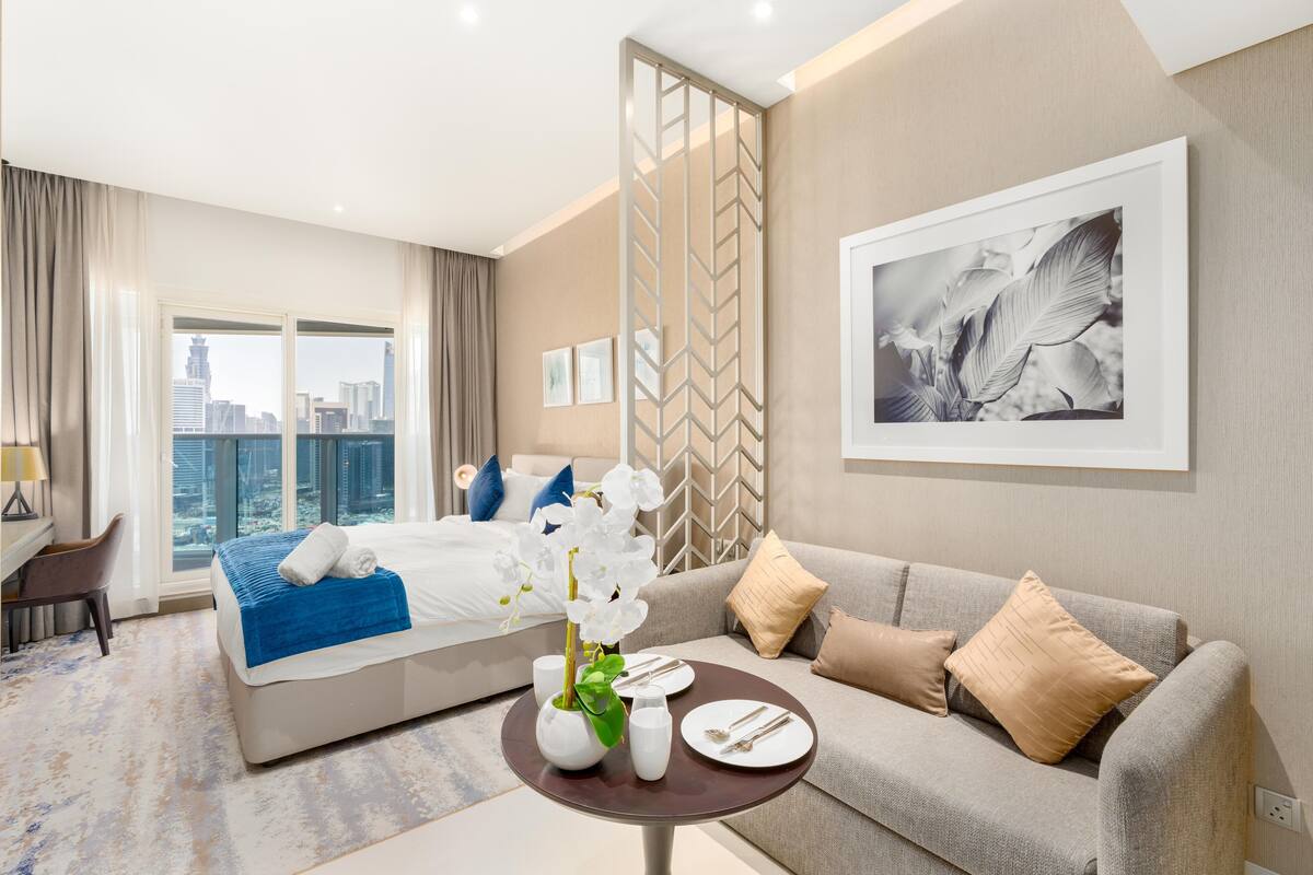 Ein modernes Hotelzimmer mit Bett, einer Couch, einem Esstisch und Blick auf die Stadt.