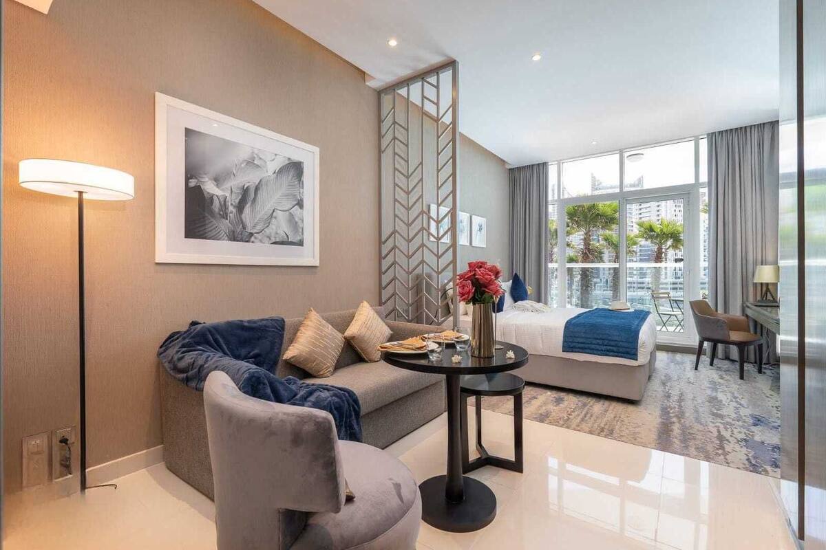 Ein modernes Hotelzimmer mit einer Couch, einem runden Tisch mit Blumenvase, einem großen Fenster mit Stadtblick und einer dekorativen Wandverkleidung.