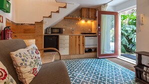 A compact living space with a kitchenette, a sofa with floral cushions, and a patterned floor. - Pendoa sintra collection-Rua da Biquinha nº7(Edifício separado) (Sintra)