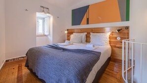 A bedroom with a wooden headboard, a bed with white linens, a grey blanket, and a painting above the bed. - Pendoa sintra collection-Rua da Biquinha nº7(Edifício separado) (Sintra)