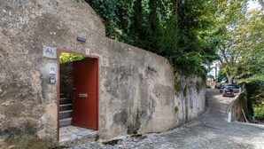 A narrow cobblestone street with a red door and a stone wall. - Pendoa sintra collection-Rua da Biquinha nº7(Edifício separado) (Sintra)