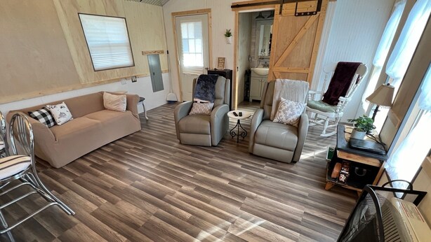 Un salon spacieux doté d’un plancher en bois, d’un canapé, de deux fauteuils, d’une petite table et d’une porte coulissante de style rustique.