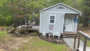 Une petite cabane avec une terrasse, un espace extérieur aménagé et couvert, et un petit étang.