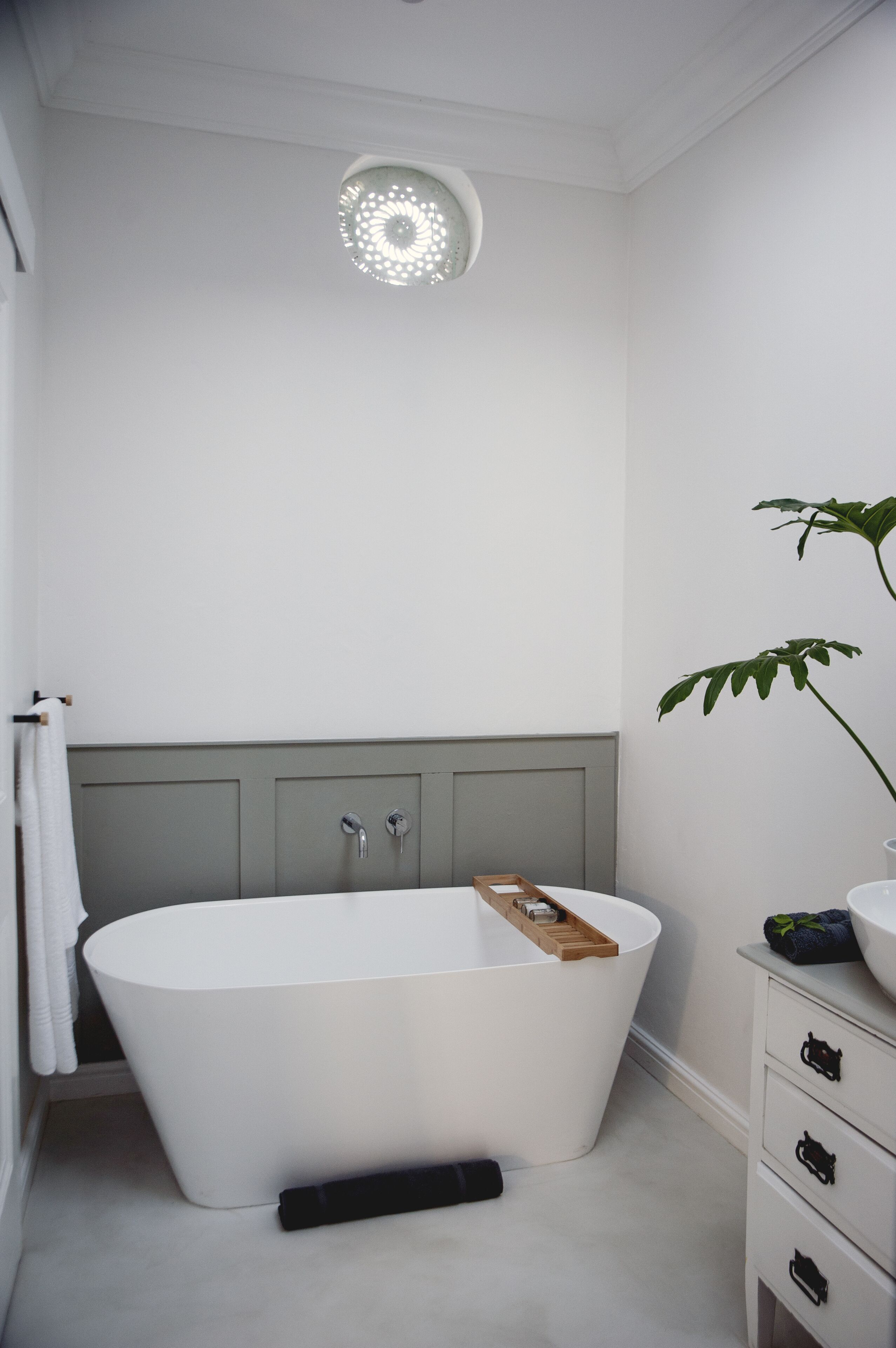 A modern bathroom with a freestanding bathtub, a towel rack, a sink, and a plant.