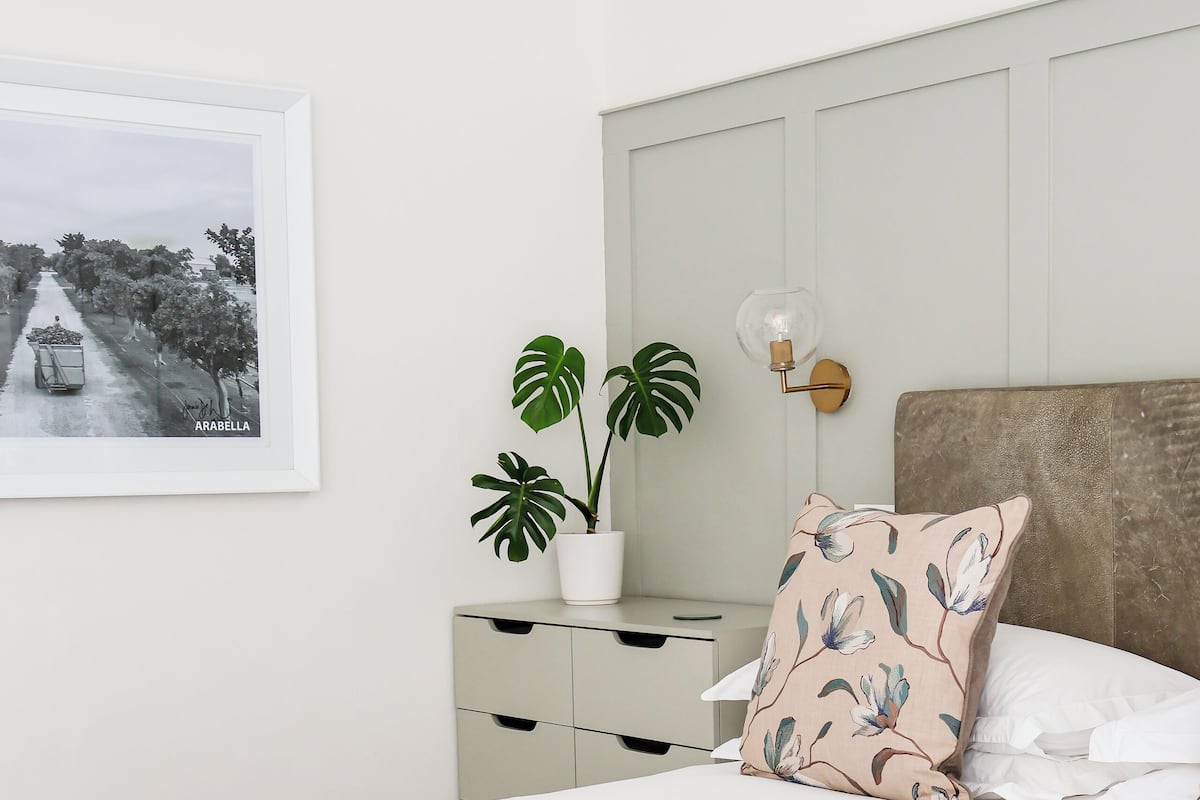 A neatly arranged bedroom with a bed, a bench, a bedside table with a plant, and a framed picture on the wall.