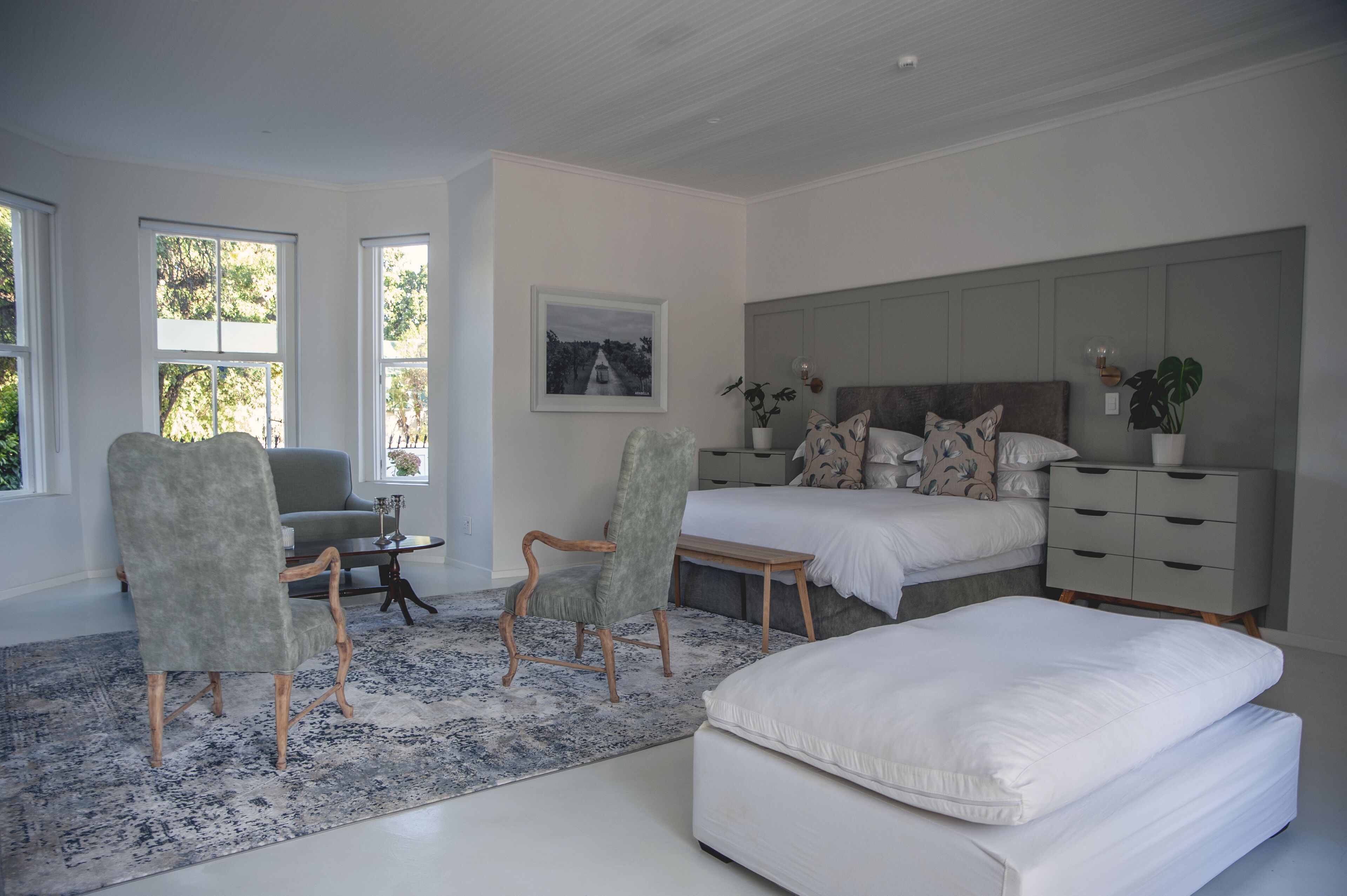 A bedroom with a large bed, two armchairs, a small table, a bedside table, and a nightstand.