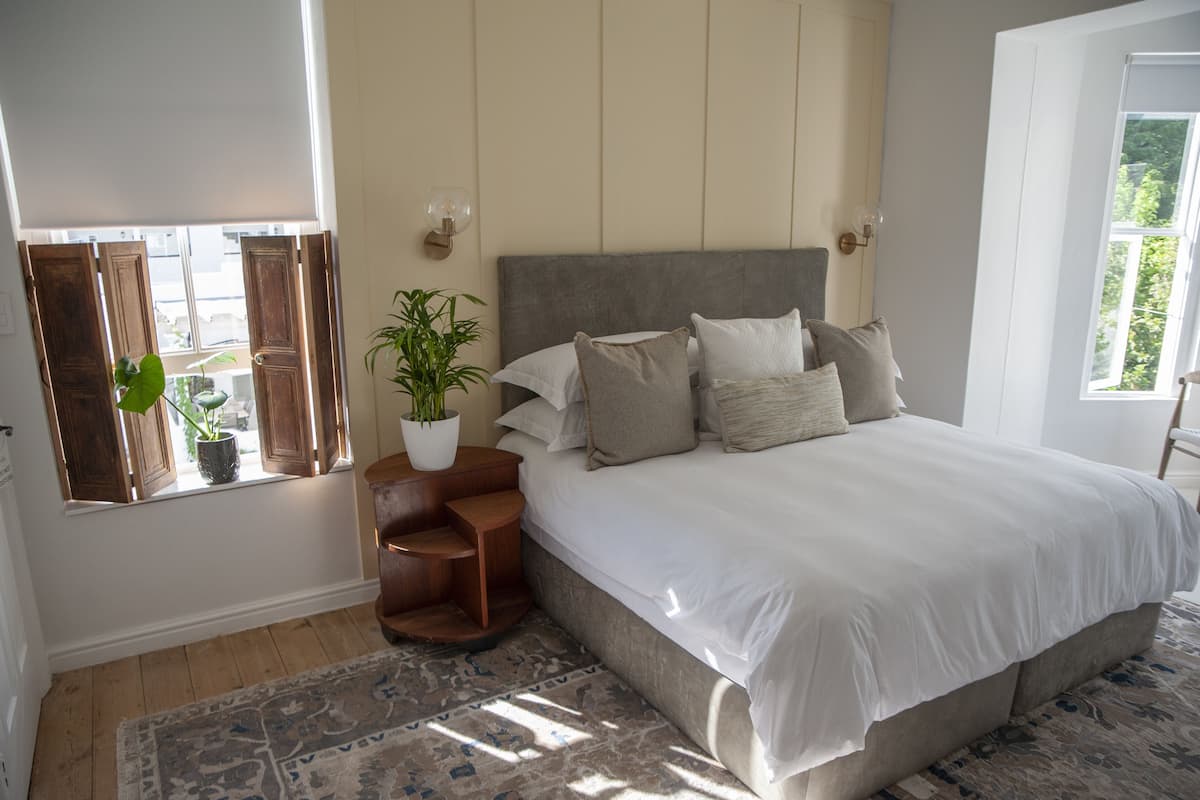 A bedroom with a large bed, a nightstand with a plant, and a window with wooden shutters.