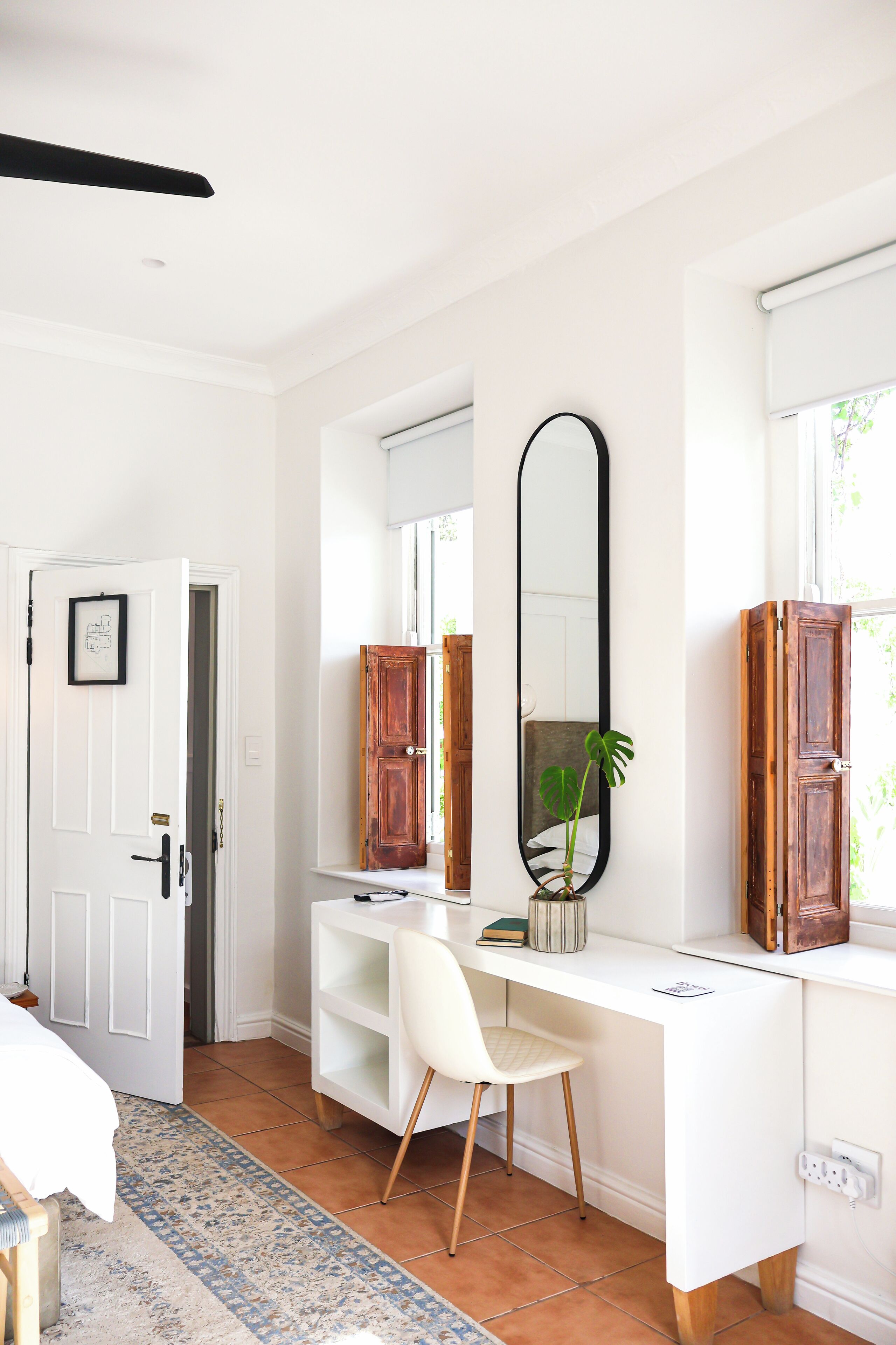 Una habitación blanca con escritorio, silla y espejos grandes.