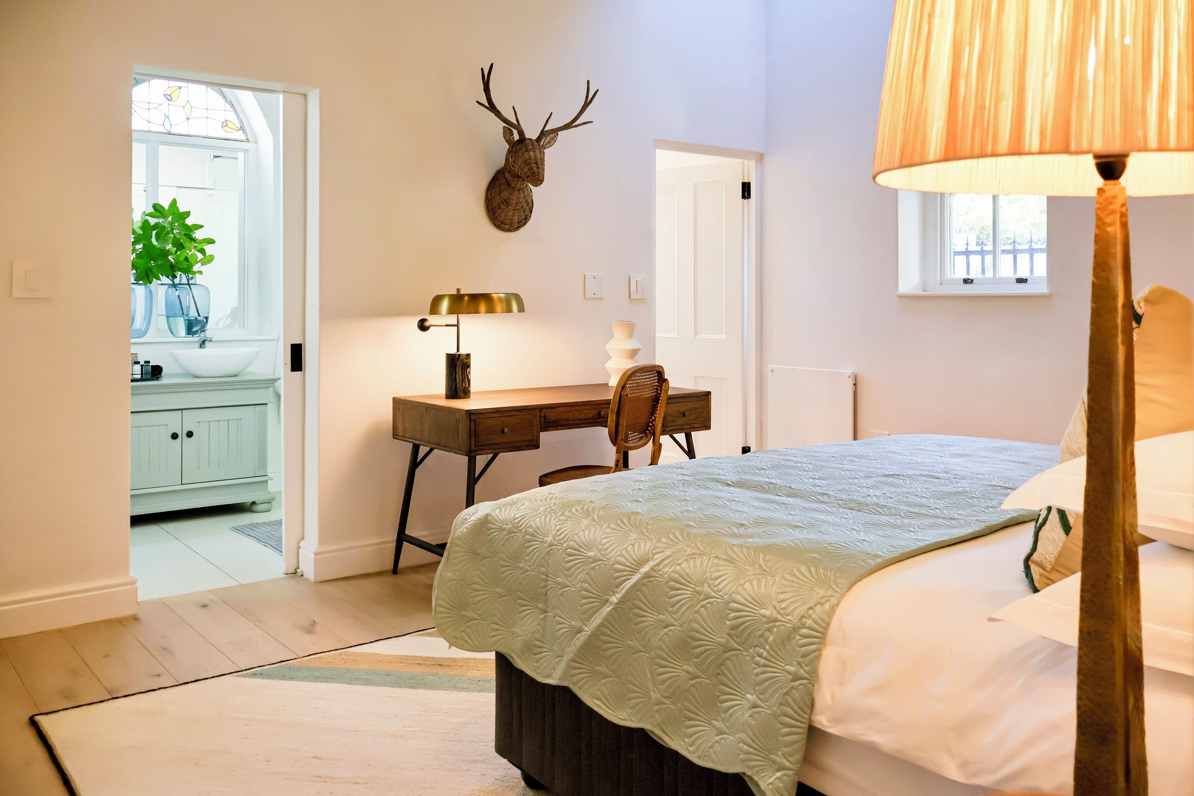 Une chambre à coucher comprenant un lit, un bureau, une chaise, une lampe et une décoration représentant une tête de cerf.