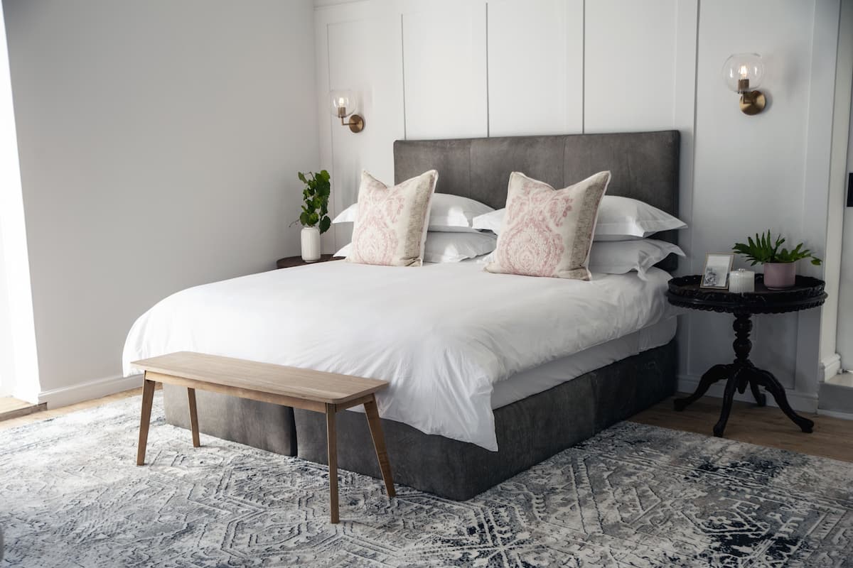 A bedroom with a large bed, bedside tables, a bench, and a patterned rug.