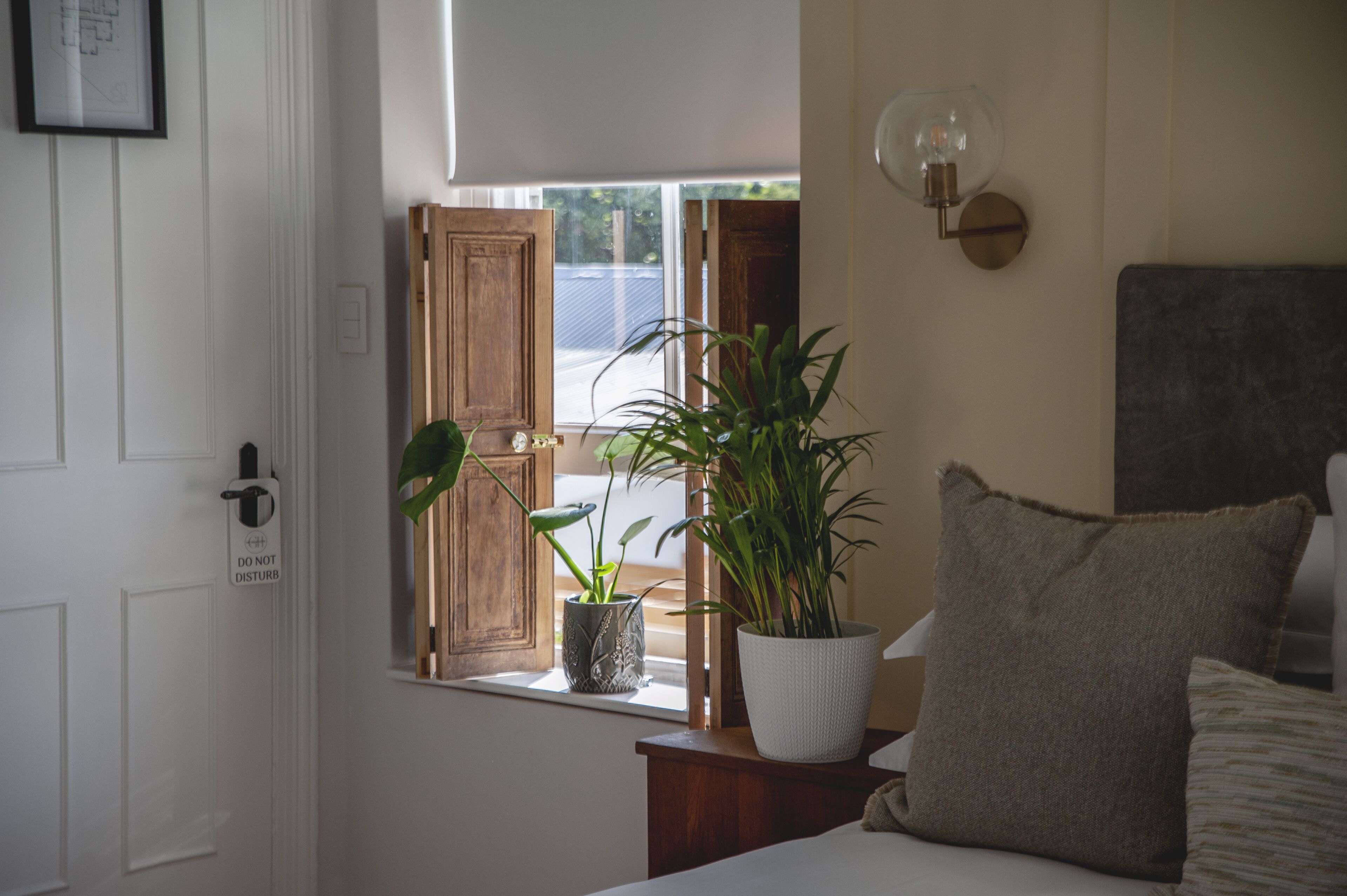 Quarto com uma cama, mesa de cabeceira, janela com vista e porta com a placa 'NÃO PERTURBE'.