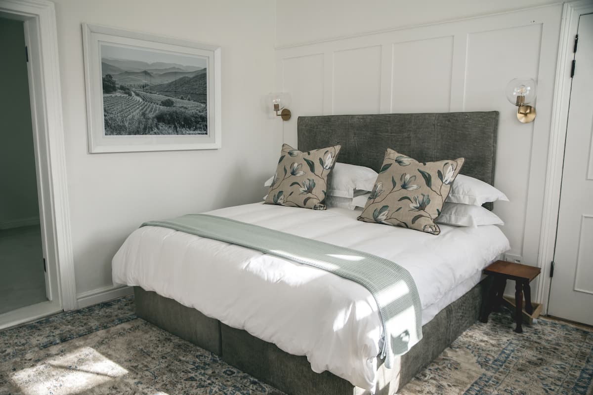 A bedroom with a large bed, a headboard, a bedside table, a nightstand, a framed picture on the wall, and a patterned rug.