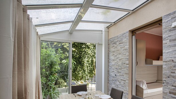 Een moderne eetruimte met glazen dak, stenen muur en uitzicht op groen.