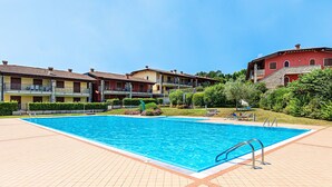Piscina com deck revestido, rodeada por edifícios com vários andares, varandas e área de jardim.