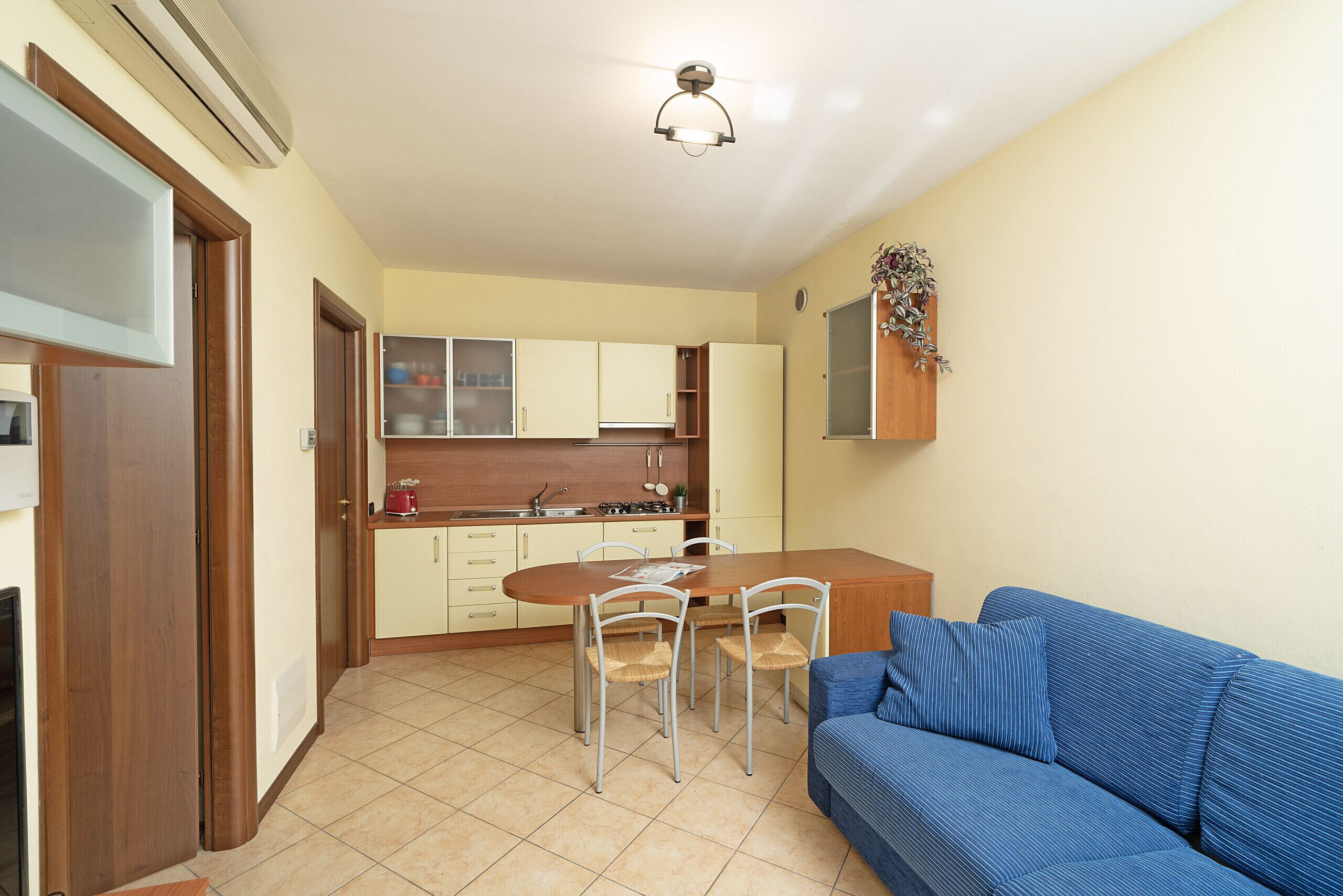A compact living space with a kitchenette, a dining area with four chairs, and a blue sofa.