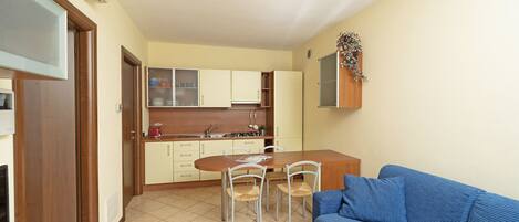 A compact living space with a kitchenette, a dining area with four chairs, and a blue sofa.