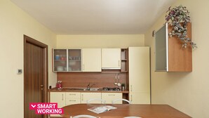 Uma cozinha compacta com área de jantar, apresentando uma mesa de madeira, cadeiras brancas e fogão embutido.