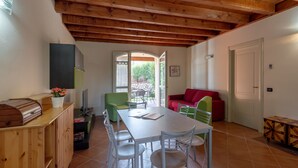 Zona pranzo con soffitto in legno, un tavolo con sedie, un divano rosso e una poltrona verde.