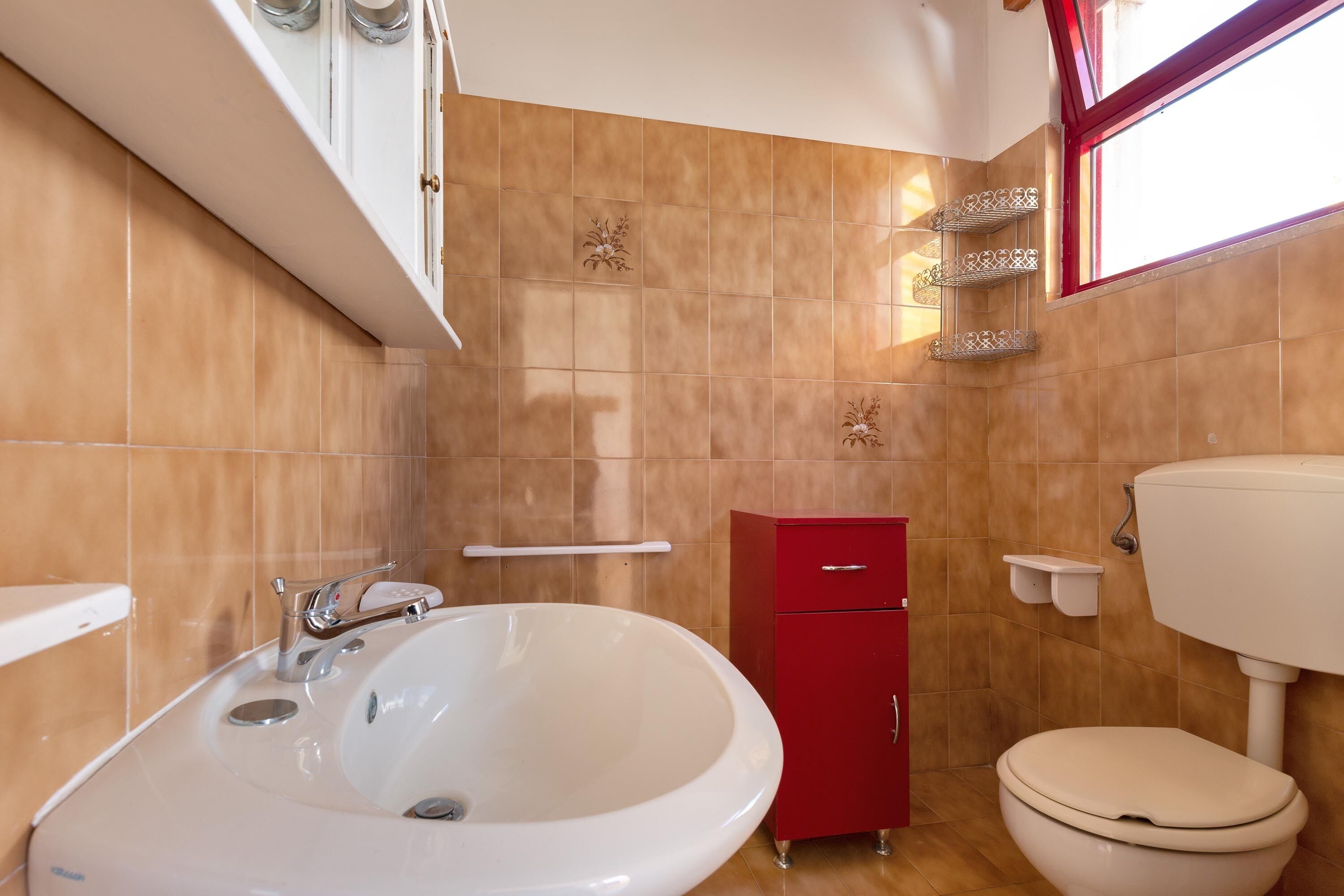 Un baño con un lavamanos grande de color blanco, un armario rojo y un inodoro.
