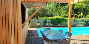 A wooden deck with a pool table and chairs, surrounded by a wooden fence and lush greenery.