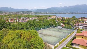 Ein Tennisplatz, umgeben von Wohnhäusern und üppiger Bepflanzung, mit einem See und Bergen im Hintergrund.
