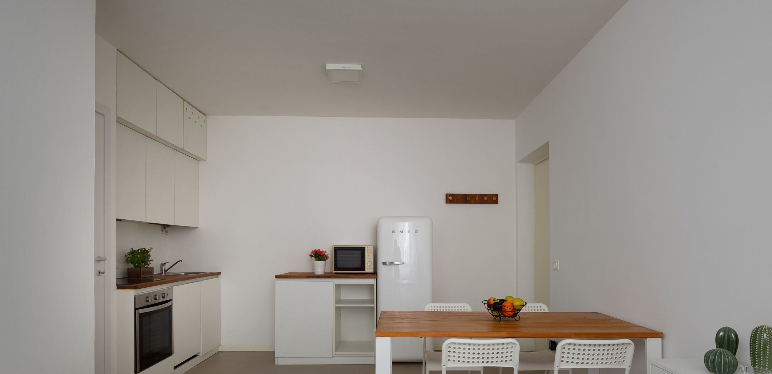 A compact kitchen with white cabinets, a microwave, a refrigerator, and a wooden dining table with chairs.