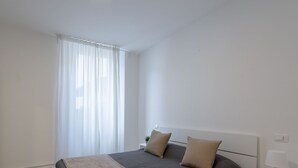 A minimalist bedroom with a bed, a nightstand, and a window with sheer curtains. - Residence Orti 18 by Wonderful Italy (Salò)