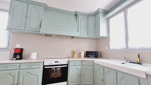 A kitchen with light green cabinets, a white countertop, a black microwave, a coffee maker, and a stove.